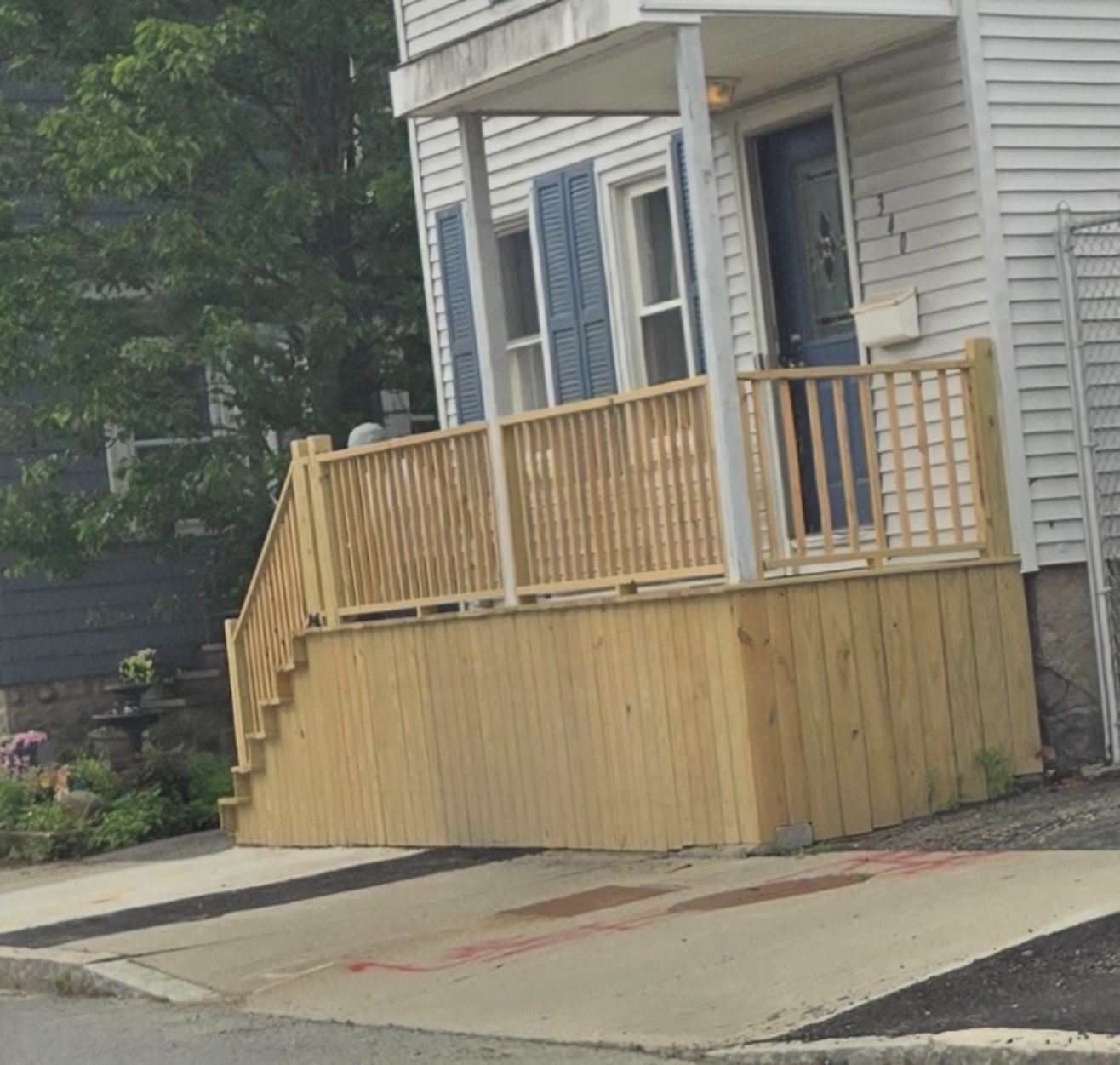 Rebuilt front porch with new wooden railings, stair rail and vertical board skirting on a white two-family house