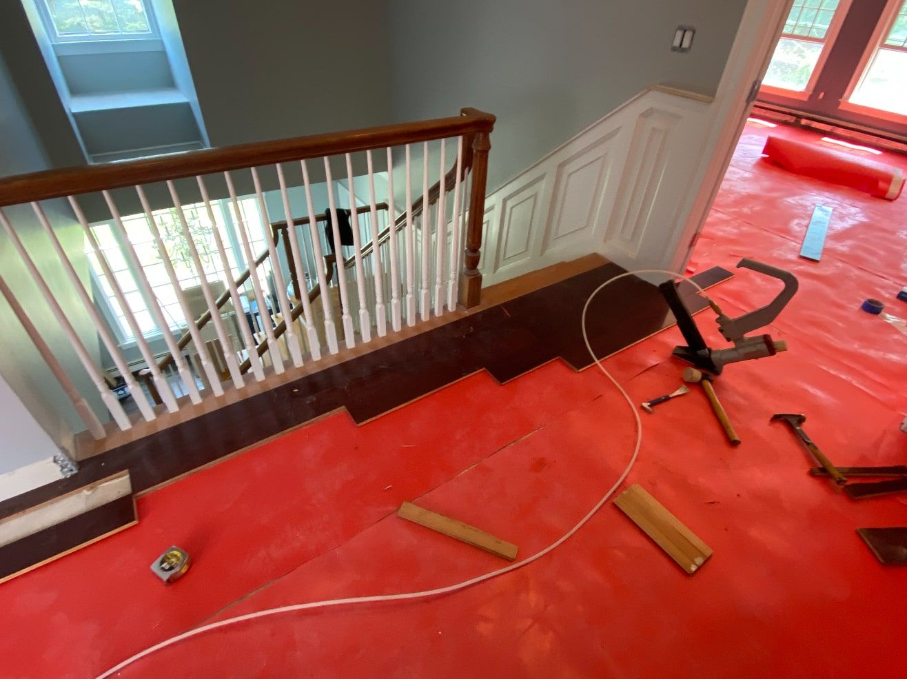 Dark hardwood flooring being installed along a stair landing with a flooring nailer, over red rosin paper