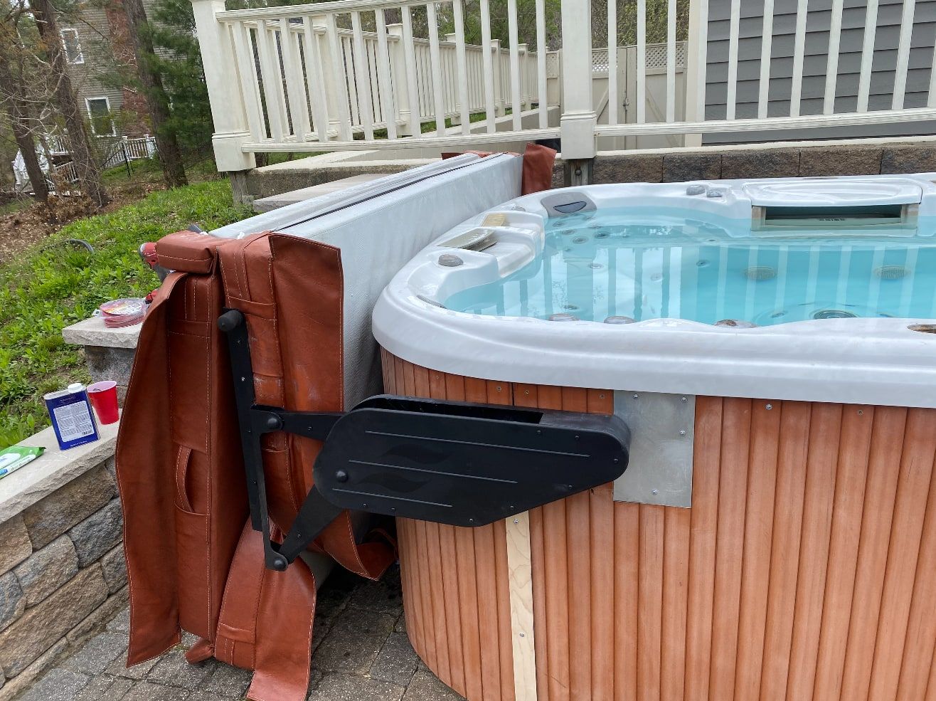 Hot tub with a newly mounted cover lifter arm holding the cover upright, on a paver patio