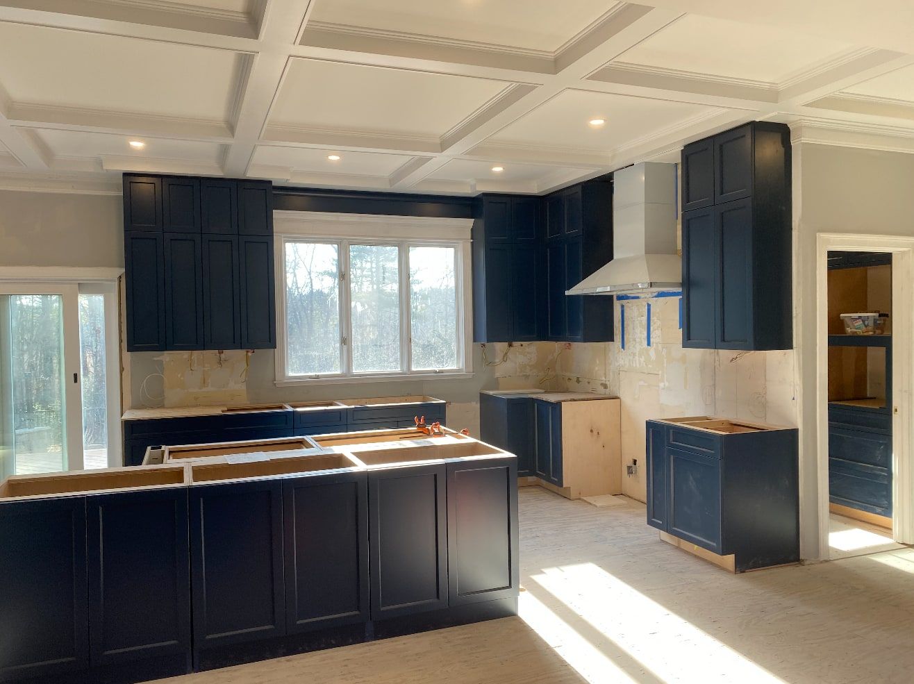 Navy shaker kitchen cabinets and island installed under a white coffered ceiling, ready for countertops