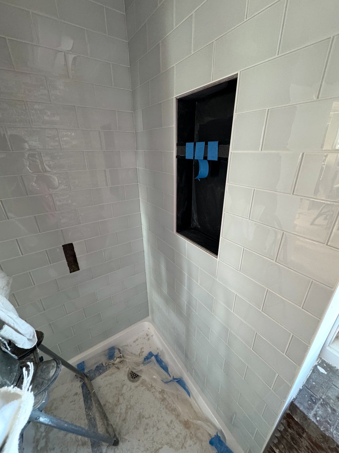 Shower walls finished in pale grey glossy subway tile with a recessed black shower niche